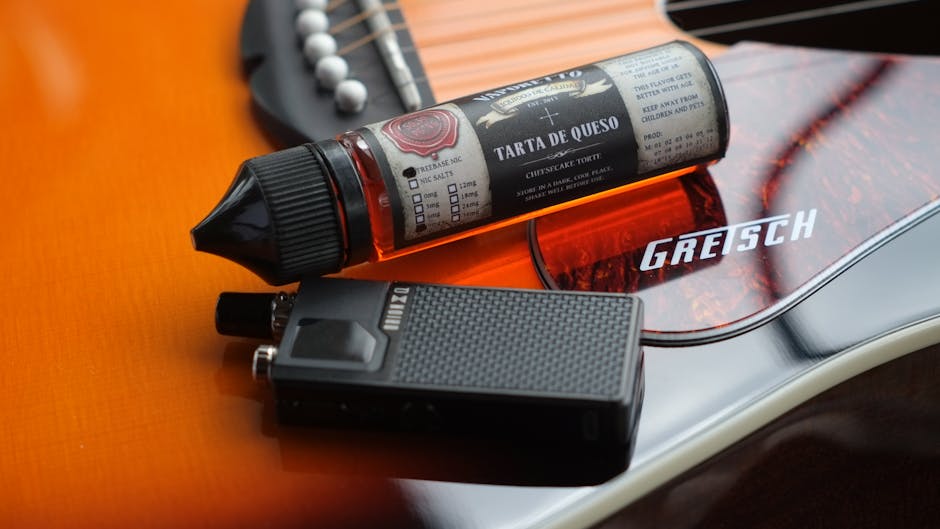Gros plan sur un liquide et un dispositif de vape posés sur une guitare Gretsch, mêlant musique et technologie moderne.